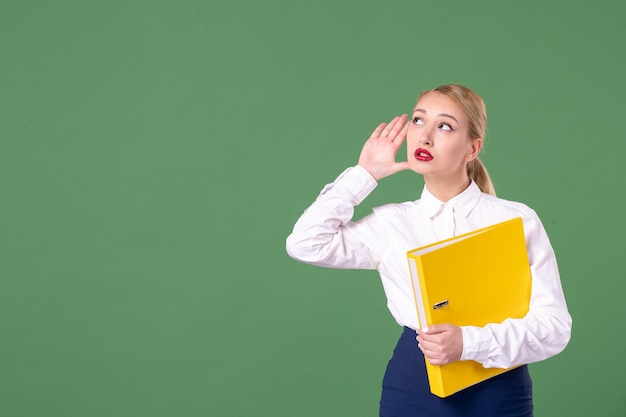 Vue de face enseignante posant avec des fichiers jaunes sur fond vert étude de la bibliothèque de l'école uniforme universitaire travail étudiant femme leçon