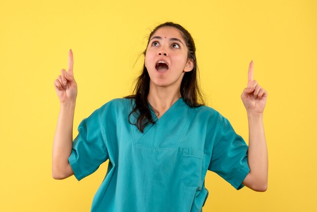 Vue de face étonné femme médecin en uniforme debout sur fond jaune