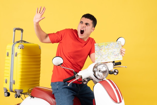 Vue de face étonné jeune homme dans des vêtements décontractés sur un cyclomoteur tenant une carte de voyage