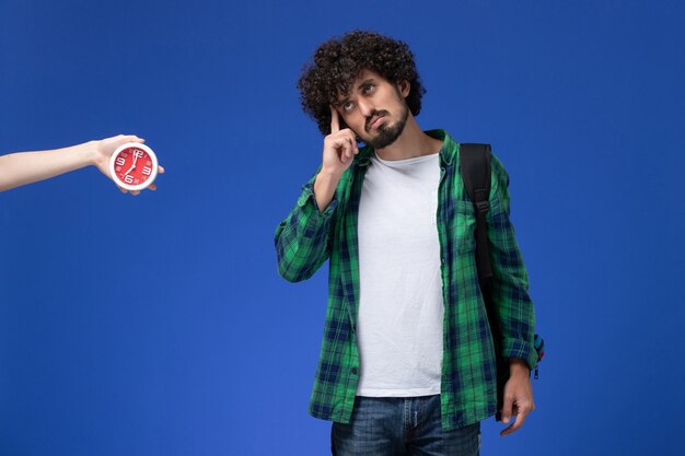 Vue de face d'un étudiant portant un sac à dos noir pensant sur un mur bleu clair