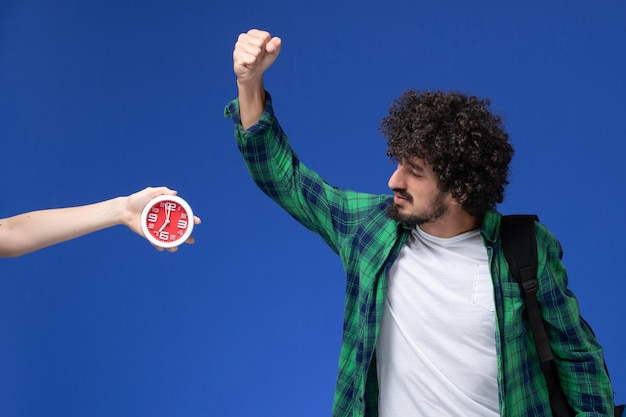 Photo gratuite vue de face de l'étudiant de sexe masculin portant un sac à dos noir posant sur un mur bleu clair