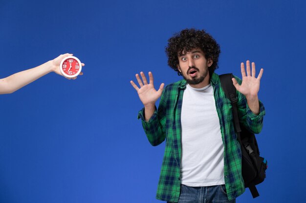 Vue de face de l'étudiant de sexe masculin portant un sac à dos noir posant sur un mur bleu clair