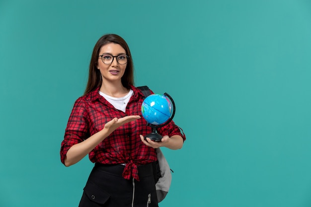 Vue de face de l'étudiante portant sac à dos tenant petit globe sur mur bleu clair