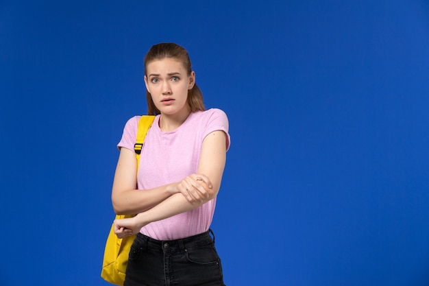 Vue de face de l'étudiante en t-shirt rose avec sac à dos jaune juste debout sur le mur bleu
