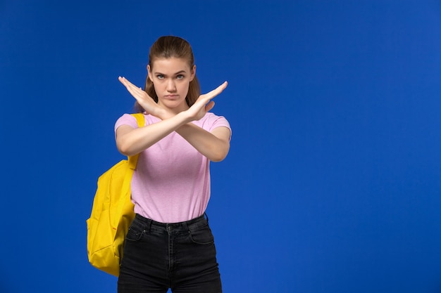 Vue de face de l'étudiante en t-shirt rose avec sac à dos jaune signe d'interdiction shwoing sur mur bleu