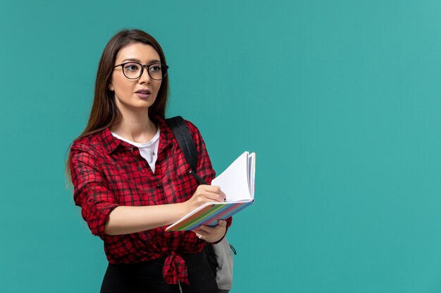 Vue de face de l'étudiante tenant un cahier et un stylo écrit sur le mur bleu clair