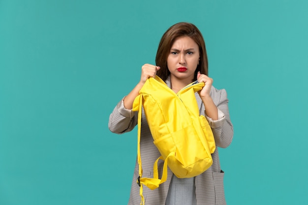 Vue De Face De L'étudiante En Veste Grise Tenant Son Sac à Dos Jaune Sur Le Mur Bleu Clair