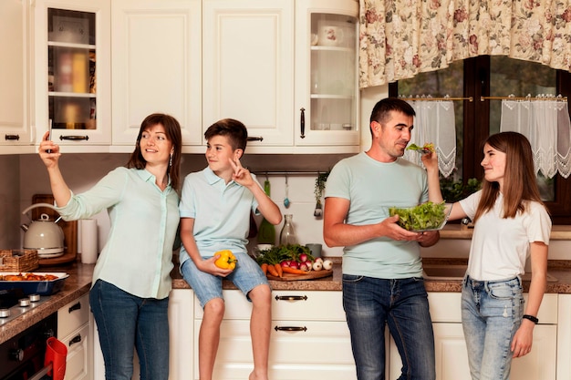 Vue de face de la famille posant avec de la nourriture dans la cuisine