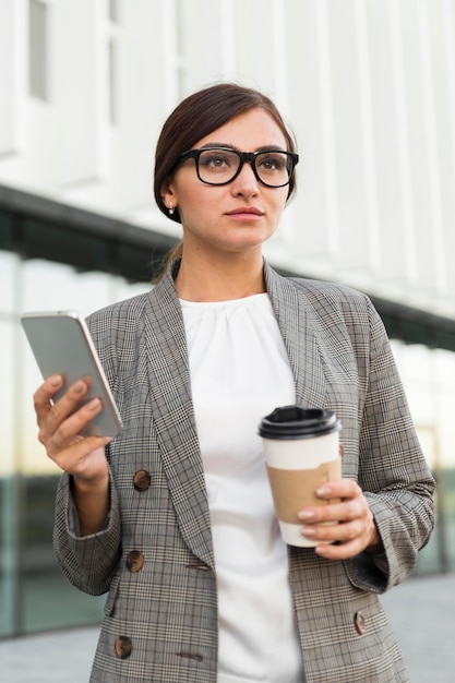 Vue de face de la femme d'affaires avec café et smartphone à l'extérieur