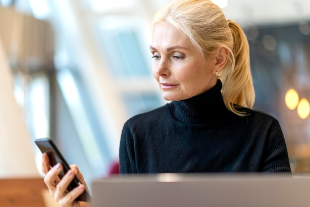 Vue de face d'une femme d'affaires plus âgée travaillant sur ordinateur portable et regardant smartphone