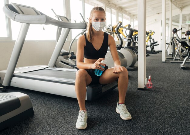 Vue de face de la femme à l'aide de désinfectant pour les mains tout en travaillant à la salle de sport