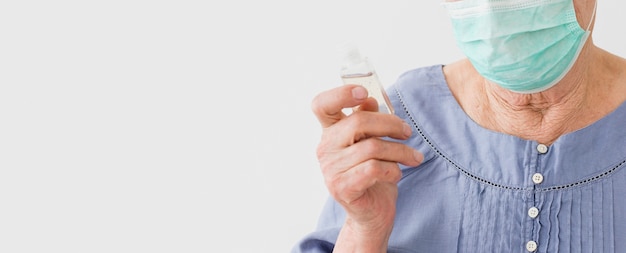 Vue de face d'une femme aînée portant un masque médical et tenant un désinfectant pour les mains