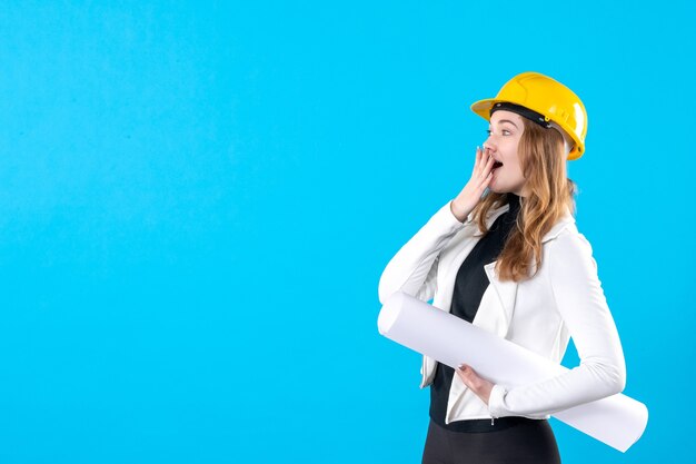 Vue de face femme architecte en casque jaune tenant plan sur bleu