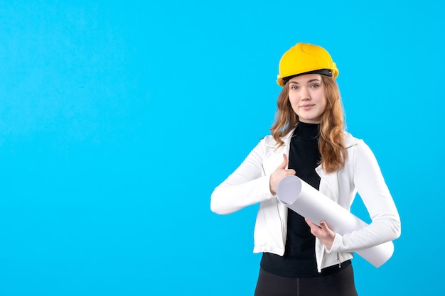 Vue de face femme architecte en casque jaune tenant plan sur bleu