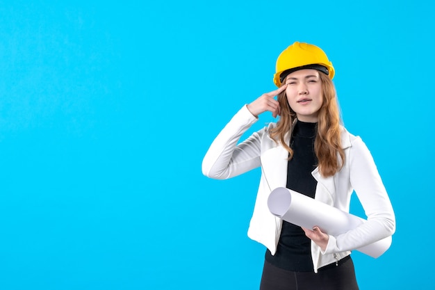 Vue de face femme architecte en casque jaune tenant plan sur bleu