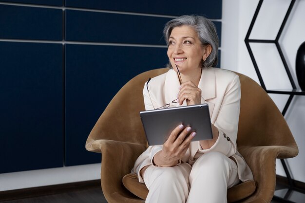 Vue de face femme assise sur une chaise avec tablette