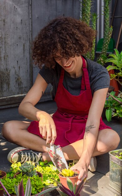 Vue de face femme assise tout en prenant soin des plantes