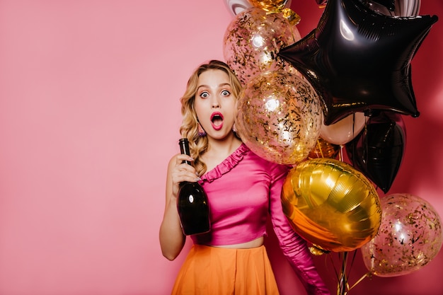 Vue de face d'une femme blonde choquée avec une bouteille de vin