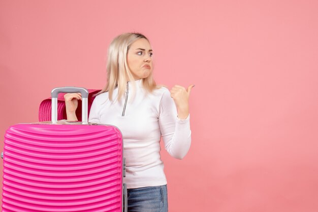 Photo gratuite vue de face femme blonde confuse debout près de valise en pointant sur quelque chose