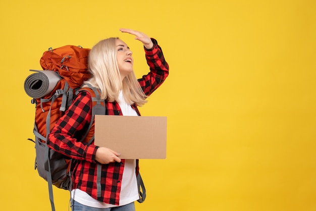 Vue de face femme blonde avec son sac à dos tenant le carton mettant la main près du front