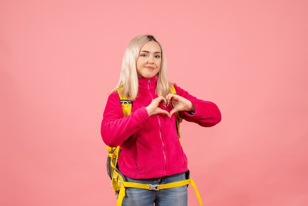 Vue de face femme blonde voyageur dans des vêtements décontractés faisant signe de coeur