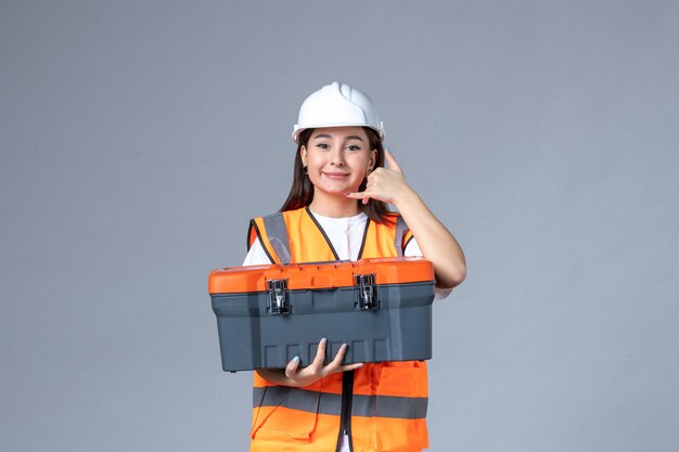 Vue de face d'une femme builder tenant une boîte à outils sur un mur gris