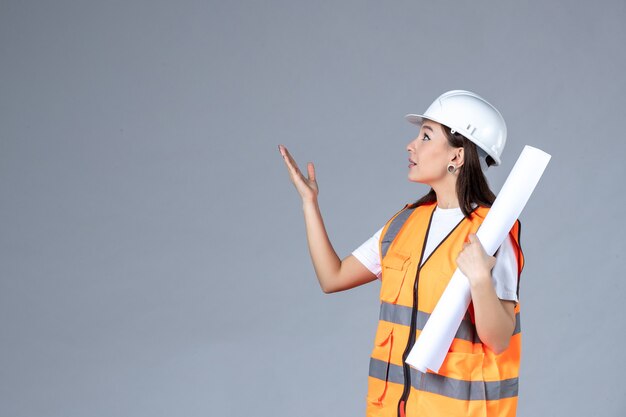 Vue de face d'une femme builder en uniforme avec une affiche dans ses mains sur un mur gris