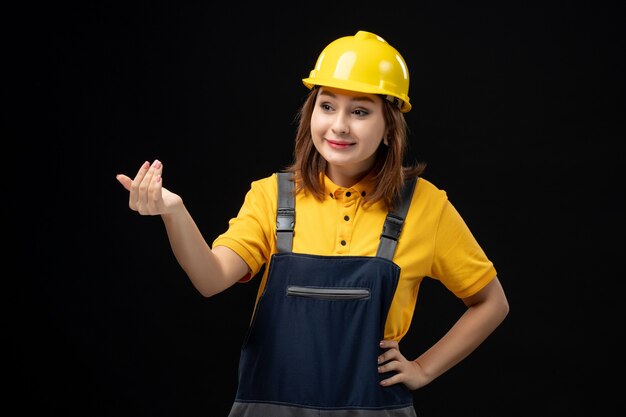 Vue de face femme builder en uniforme et casque appelant quelqu'un sur un mur noir