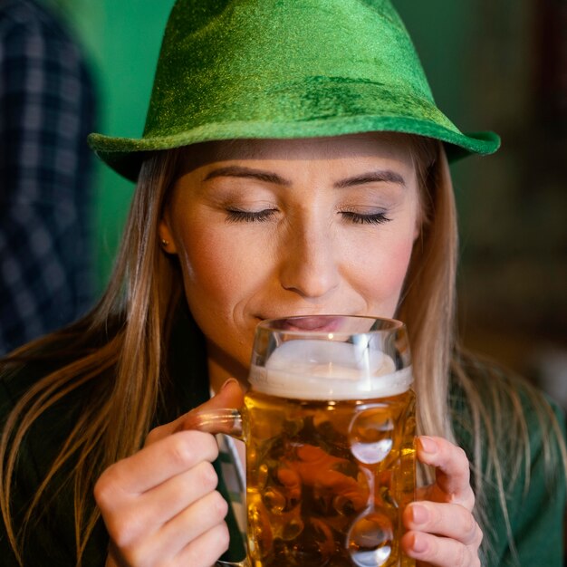 Vue de face de la femme avec chapeau célébrant st. jour de patrick avec boisson