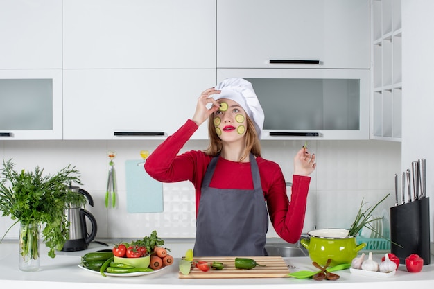 Vue de face femme chef en chapeau de cuisinier mettant des tranches de concombre sur son visage