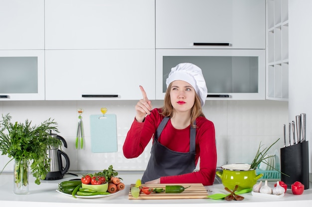 Vue de face femme chef en chapeau de cuisinier pointant quelque chose du doigt