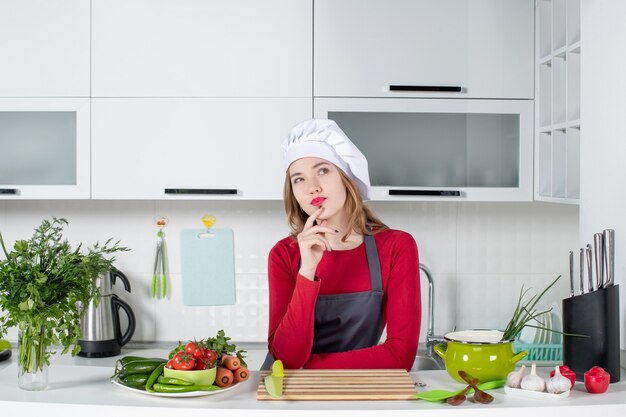 Vue de face femme chef en uniforme debout derrière la table de la cuisine