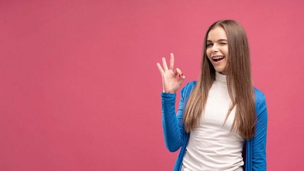 Vue de face de femme un clin de œil et donnant signe ok