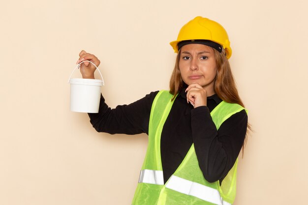 Vue de face femme constructeur en chemise noire casque jaune tenant la peinture et la réflexion sur l'architecte constructeur femme bureau blanc
