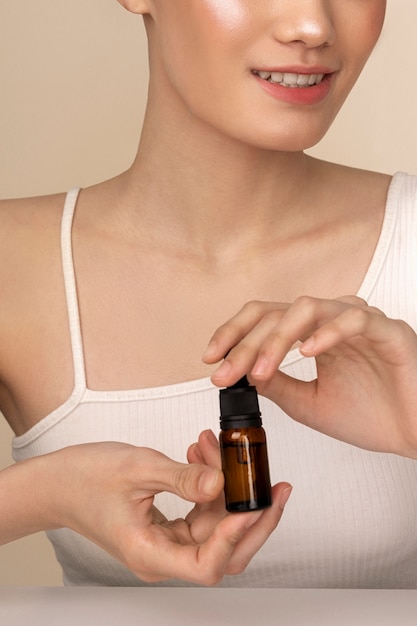 Vue de face femme coréenne posant avec une bouteille de sérum