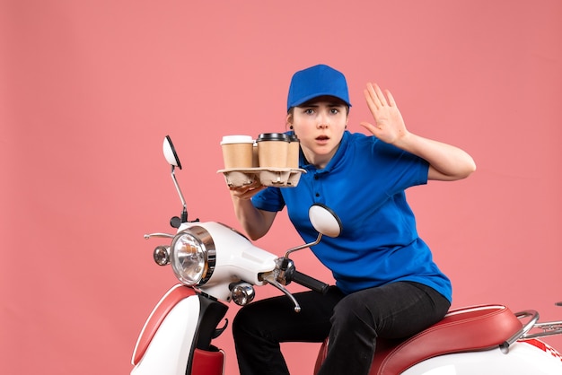 Vue de face femme courrier assis sur le vélo avec des tasses de café sur la livraison de service de travailleur uniforme de couleur de travail rose