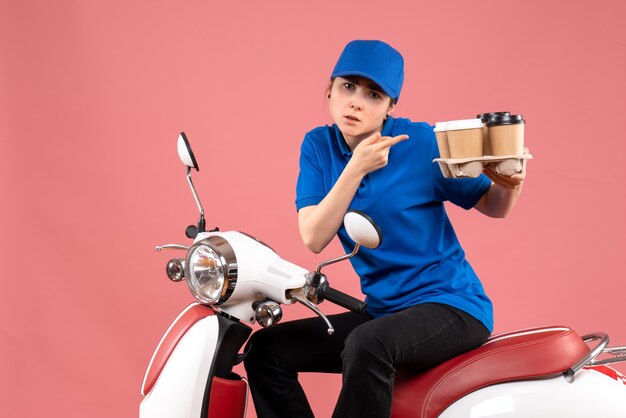 Vue de face femme courrier assis sur le vélo avec des tasses de café sur l'uniforme de couleur rose travail travailleur service alimentaire