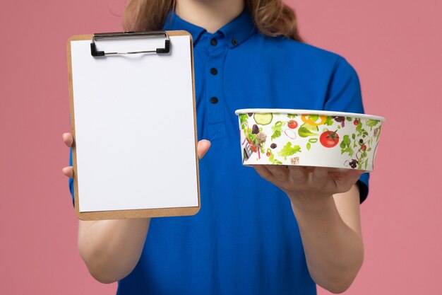 Vue de face femme courrier en cape uniforme bleu tenant le bloc-notes et le bol de livraison sur le mur rose, emploi d'employé de prestation de services