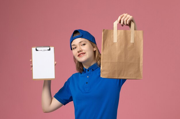 Vue De Face Femme Courrier En Cape Uniforme Bleu Tenant Le Colis De Livraison Et Le Bloc-notes Sur Le Mur Rose, La Livraison Des Emplois De Service Aux Employés