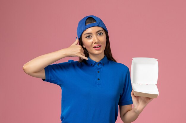 Vue de face femme courrier en cape uniforme bleu tenant des petits colis de livraison vides sur mur rose, employé de livraison de l'entreprise de services