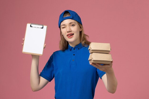 Vue de face femme courrier en cape uniforme bleu tenant peu de colis alimentaires de livraison et bloc-notes clignotant sur fond rose employé du service de livraison