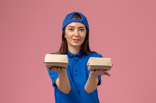 Vue de face femme courrier en cape uniforme bleu tenant peu de colis de livraison sur le mur rose, la livraison des employés de service