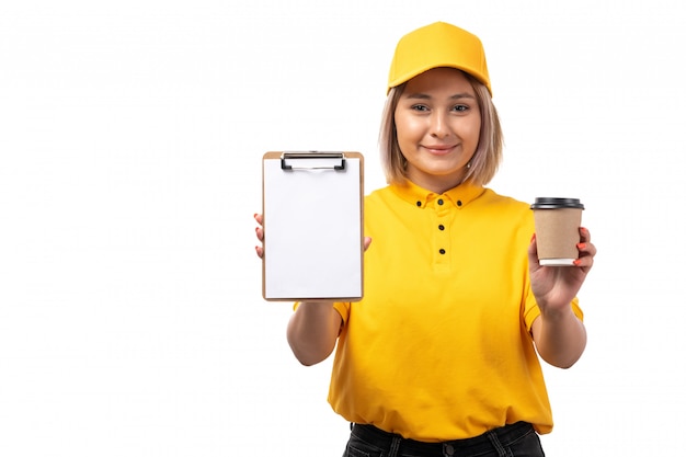 Une vue de face femme courrier en chemise jaune casquette jaune et jean noir tenant une tasse de café et bloc-notes sur blanc