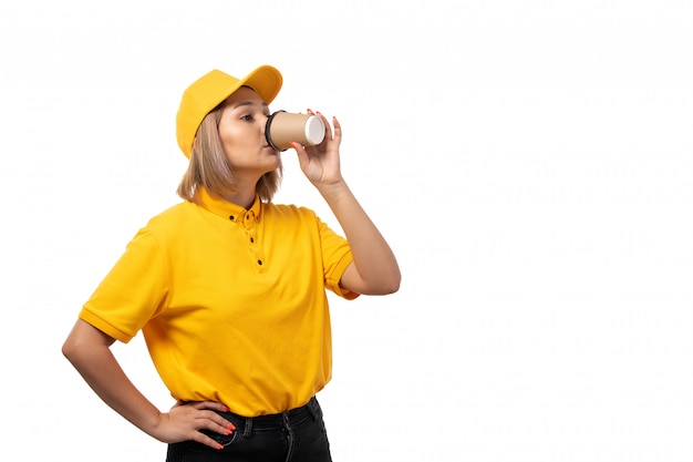 Une vue de face femme courrier en chemise jaune casquette jaune et jeans noirs de boire du café sur blanc