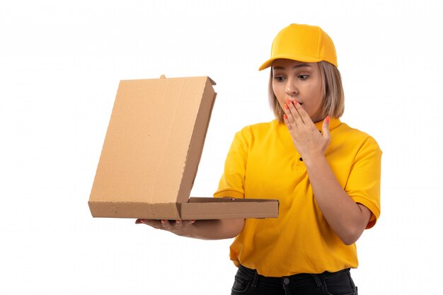 Une vue de face femme courrier en chemise jaune casquette jaune jeans noirs tenant une boîte à pizza choqué sur blanc