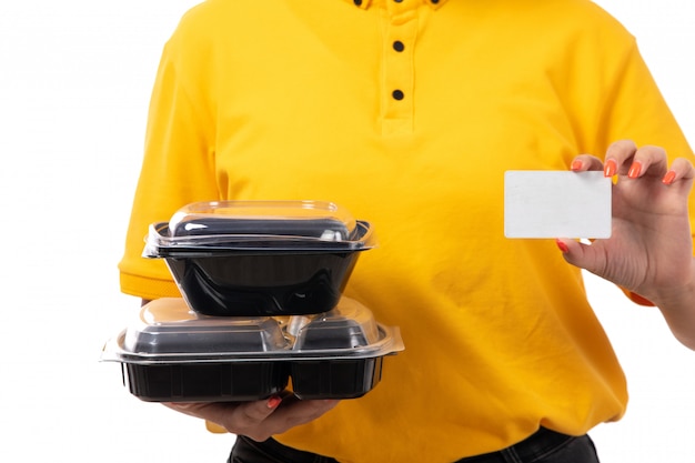 Une vue de face femme courrier en chemise jaune casquette jaune jeans noirs tenant des bols avec de la nourriture et carte blanche sur blanc