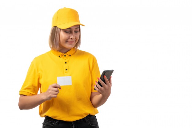 Une vue de face femme courrier en chemise jaune casquette jaune jeans noirs tenant un smartphone carte blanche sur blanc