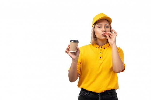 Une vue de face femme courrier en chemise jaune casquette jaune et jeans noirs tenant une tasse de café sur fond blanc livraison boisson fille