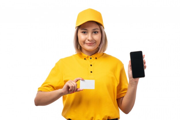 Une vue de face femme courrier en chemise jaune et casquette jaune tenant une carte blanche et un smartphone sur blanc