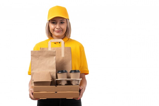 Une vue de face femme courrier en chemise jaune casquette jaune tenant des paquets et des boîtes souriant sur blanc